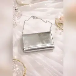 Elegant metallic silver clutch bag featuring a sleek fold-over design and detachable chain strap.